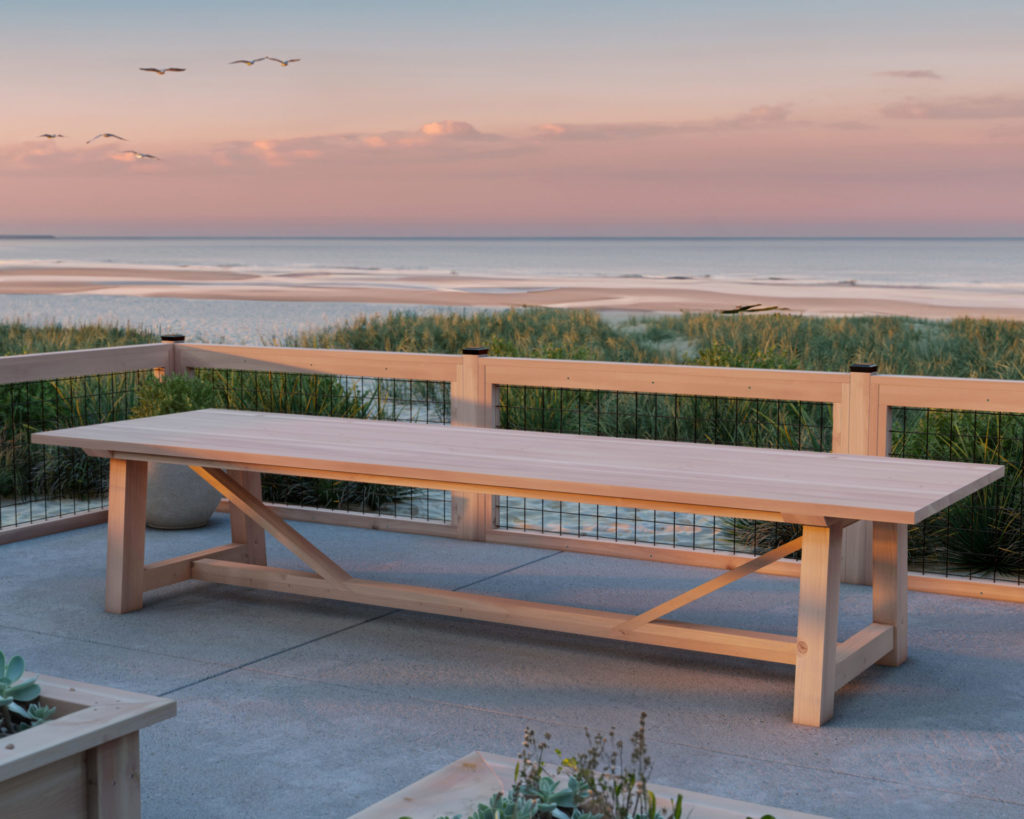 Spacious DIY farmhouse-style table overlooking a serene beach landscape at sunset.