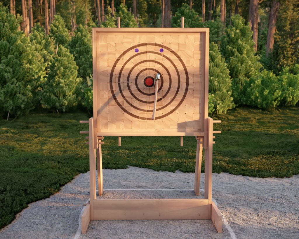DIY wooden axe throwing target in outdoor setting with lush greenery and cabin in the background.