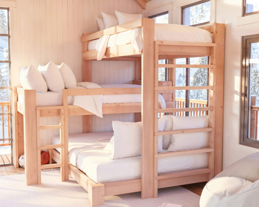 Spacious triple bunk bed with twin and queen mattresses in a sunny room with wooden flooring and scenic window view.