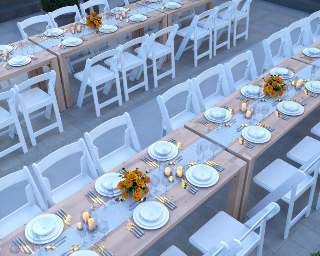 Elegant DIY wooden folding event table paired with white resin chairs set for an outdoor celebration at dusk.