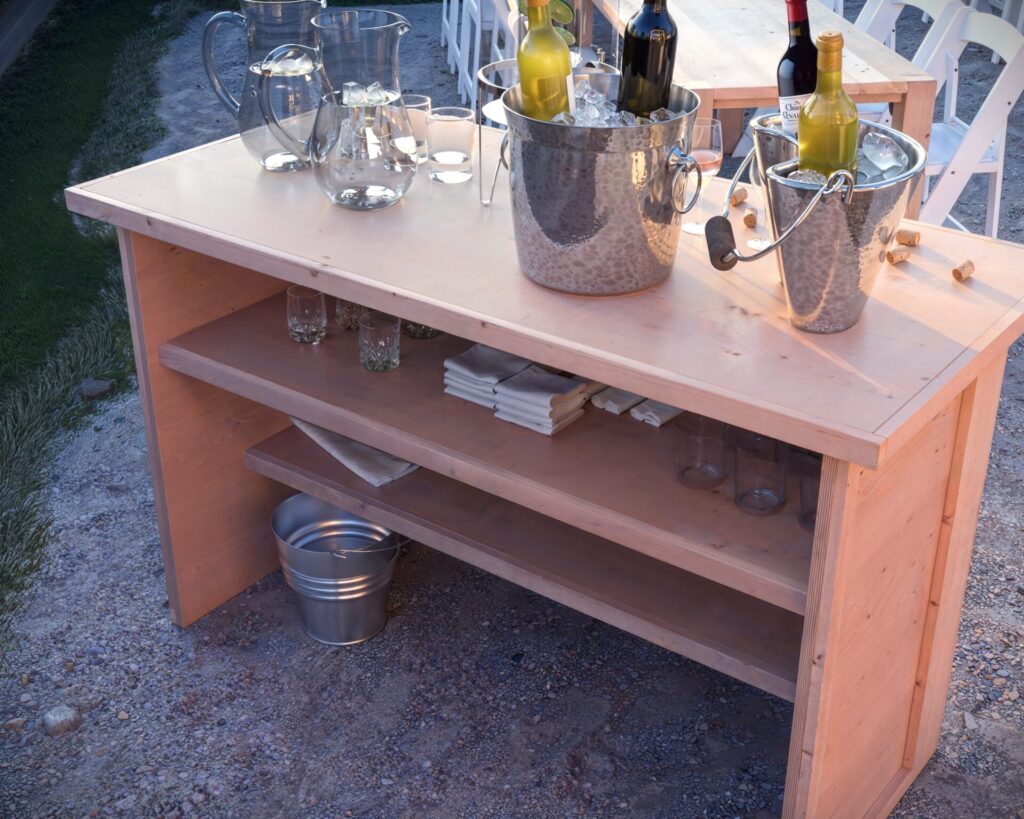 A beautifully crafted collapsible coffee bar with a wooden chevron pattern, featuring 'good vibes only' in white lettering, set up for an outdoor party with wine bottles, ice buckets, and glassware.