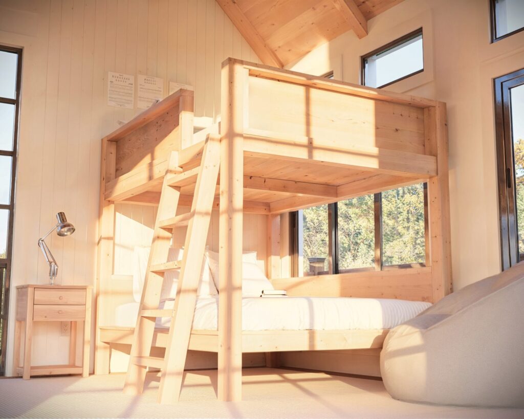 Spacious and well-lit room featuring a full over full wooden bunk bed with a simple, sturdy ladder.