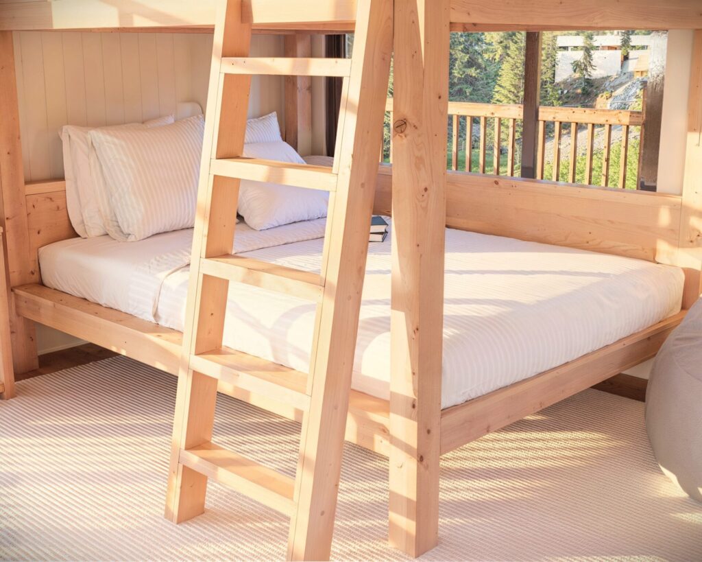 Spacious and well-lit room featuring a full over full wooden bunk bed with a simple, sturdy ladder.