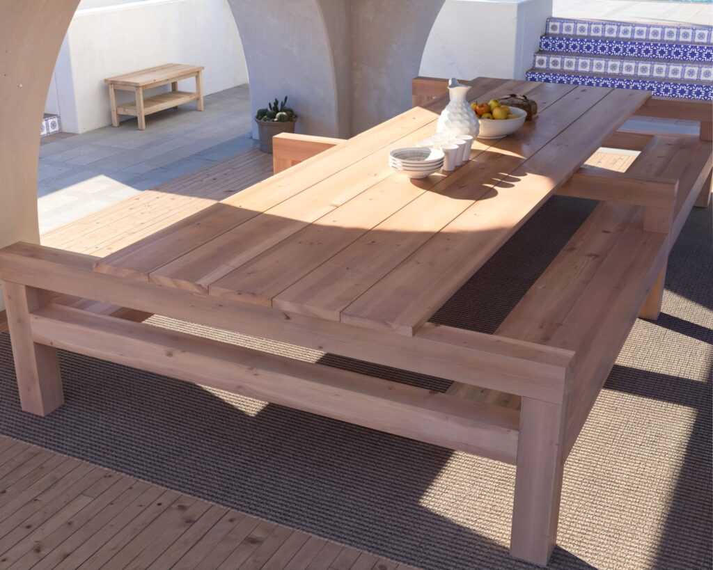 DIY wooden outdoor dining table with benches in a beautiful coastal setting, showcasing natural unfinished wood and robust construction.