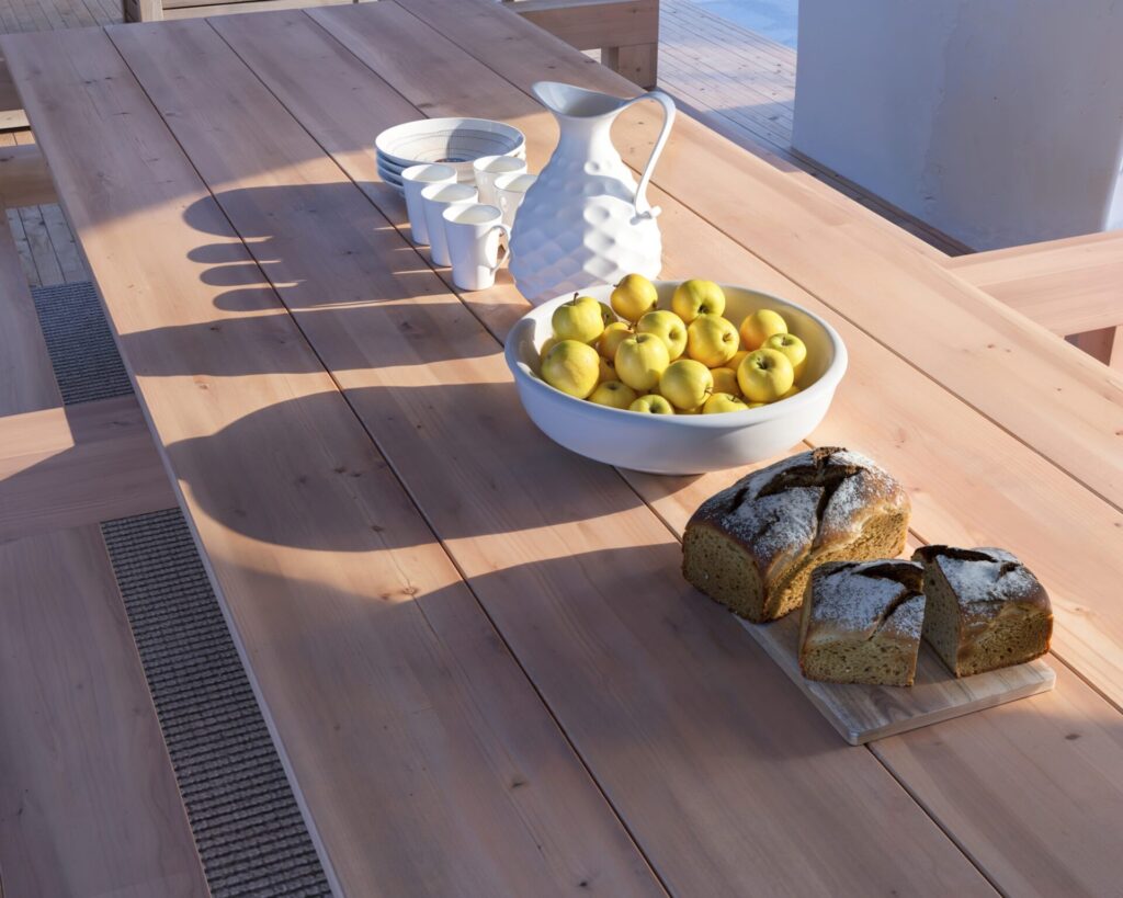 DIY wooden outdoor dining table with benches in a beautiful coastal setting, showcasing natural unfinished wood and robust construction.