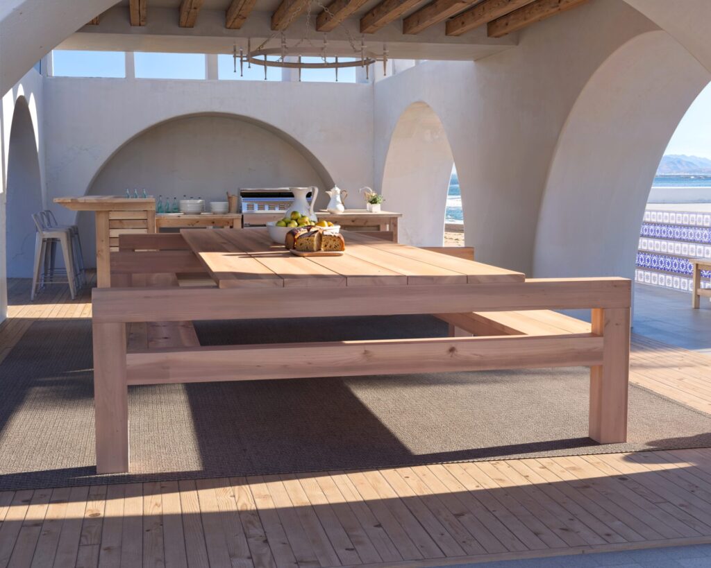 DIY wooden outdoor dining table with benches in a beautiful coastal setting, showcasing natural unfinished wood and robust construction.