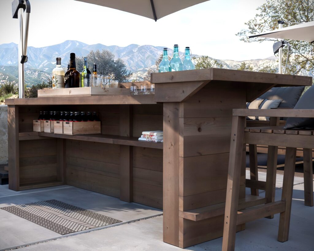 DIY L-shaped outdoor home bar made from common dimensional lumber, featuring a serving counter, adjustable shelf, and seating for four.