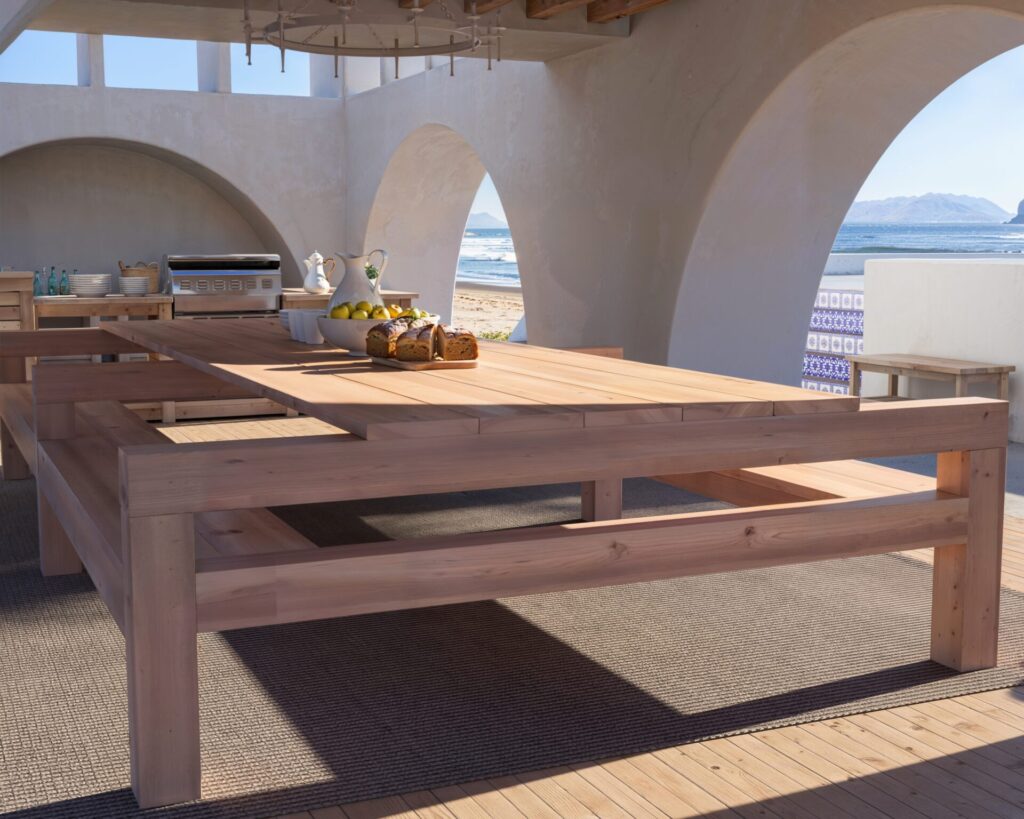 DIY wooden outdoor dining table with benches in a beautiful coastal setting, showcasing natural unfinished wood and robust construction.