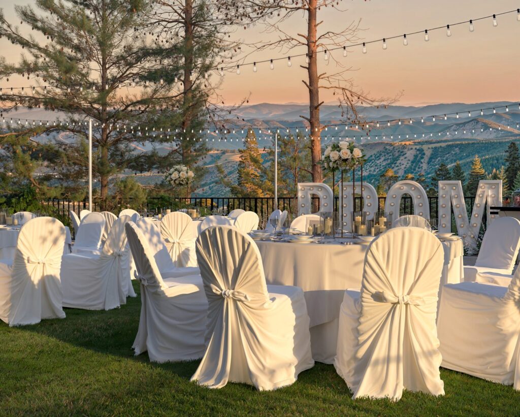 Elegant outdoor prom event with a folding event bar displaying desserts, surrounded by beautifully decorated tables, illuminated ‘PROM’ letters, and scenic mountain views.